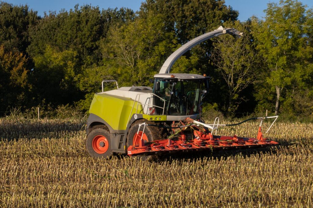 A modern tractor plowing a cornfield in the countryside with green trees in the background.