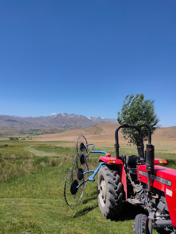Red tractor in a vast agricultural landscape under clear blue skies with mountains in the background.